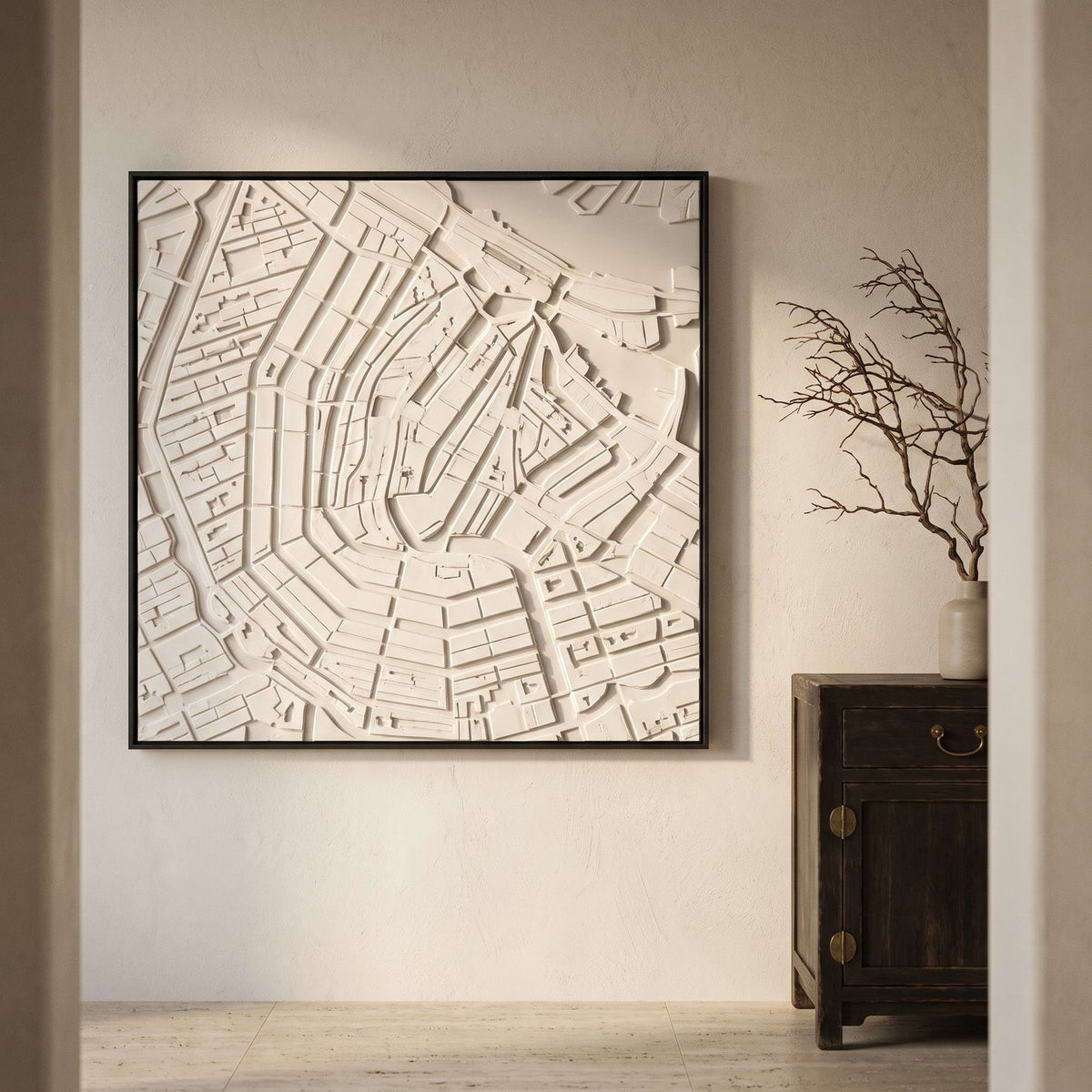 Ingelijst wandpaneel met een stadsplattegrond in wit reliëf, bouwblokken omhoog en grachten verdiept, in een hal met een donkere kast